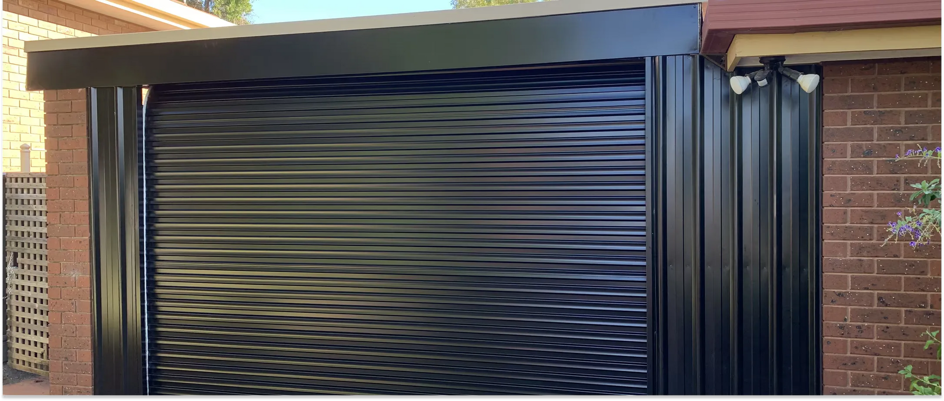 Black roll-up shutter on a brick building with a protruding frame.