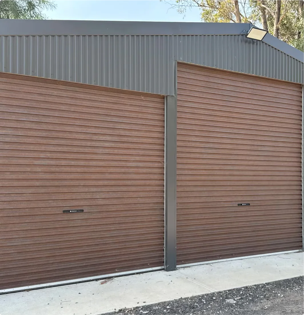 Two brown horizontal panel garage doors on a gray metal building with a concrete base.